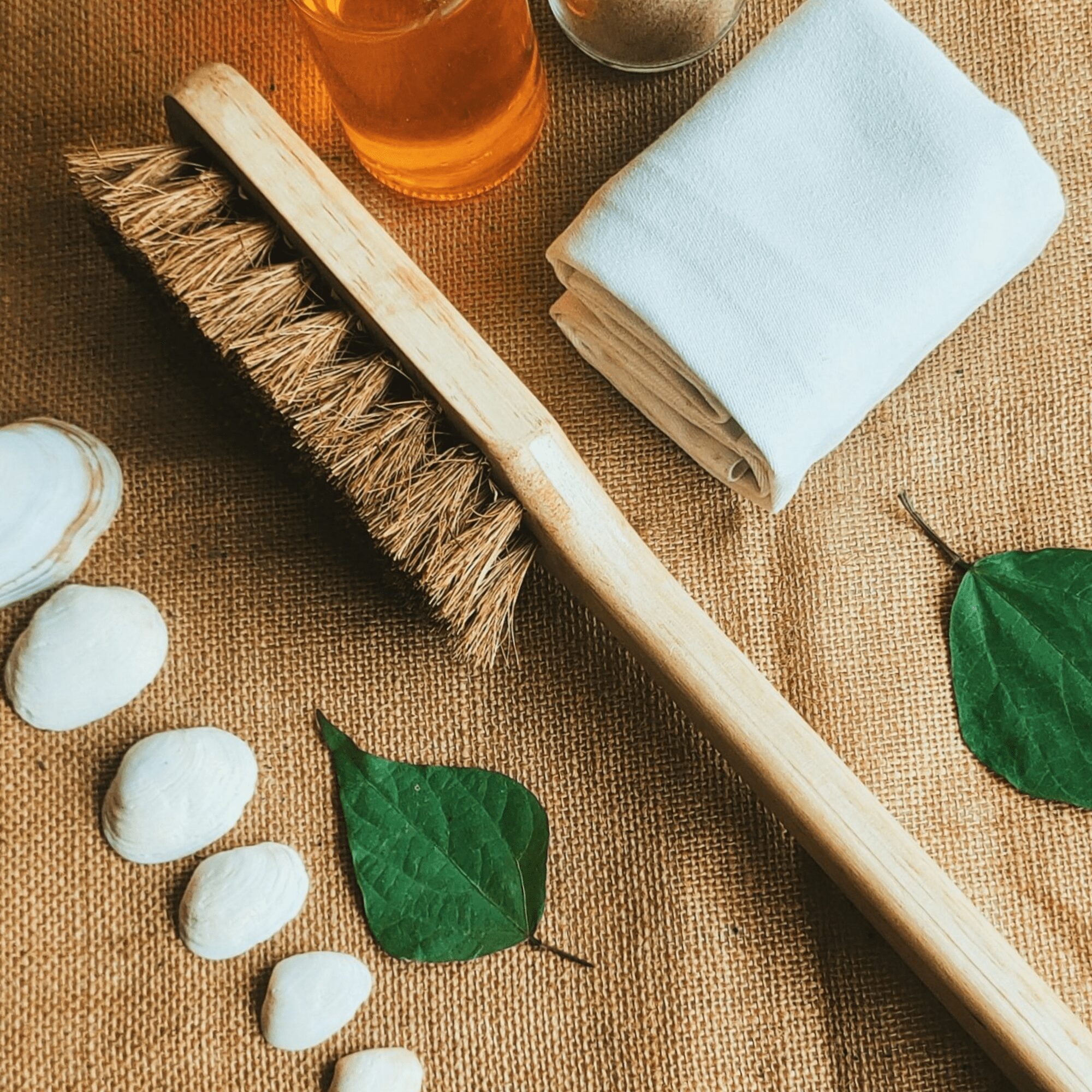 Natural long-handled wooden body brush with coir bristles, towel, and eco accents on jute background.